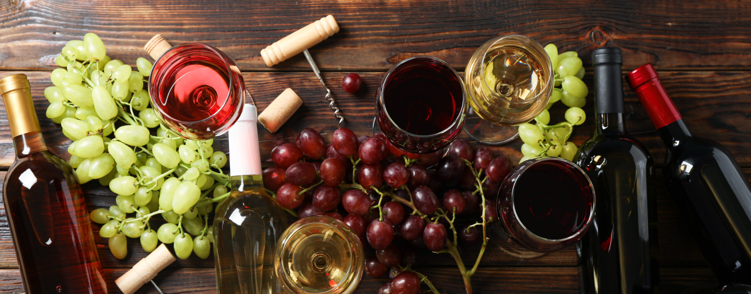 Flat lay. Grapes, corkscrew, bottles and glasses with wine on wooden background