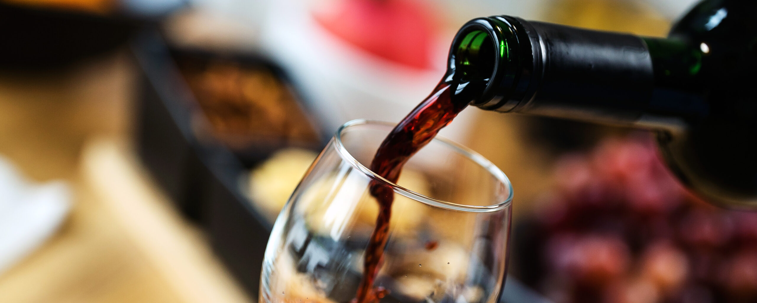 Red wine pouring into a wine glass at a tasting with various typ